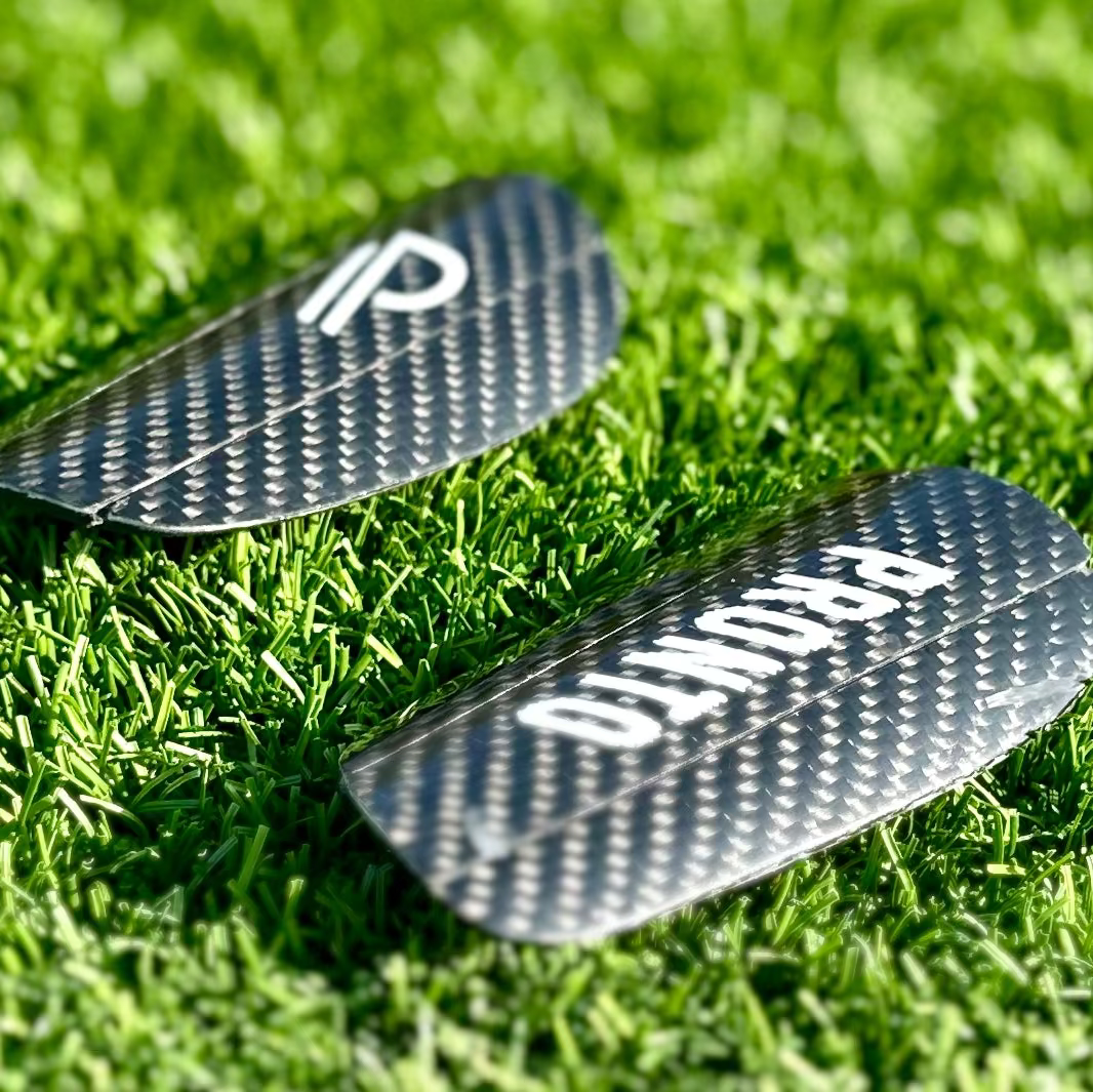 To Pronto carbon benskinner med hvide logoer placeret på grøn græsbane