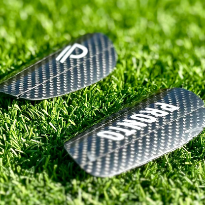 To Pronto carbon benskinner med hvide logoer placeret på grøn græsbane