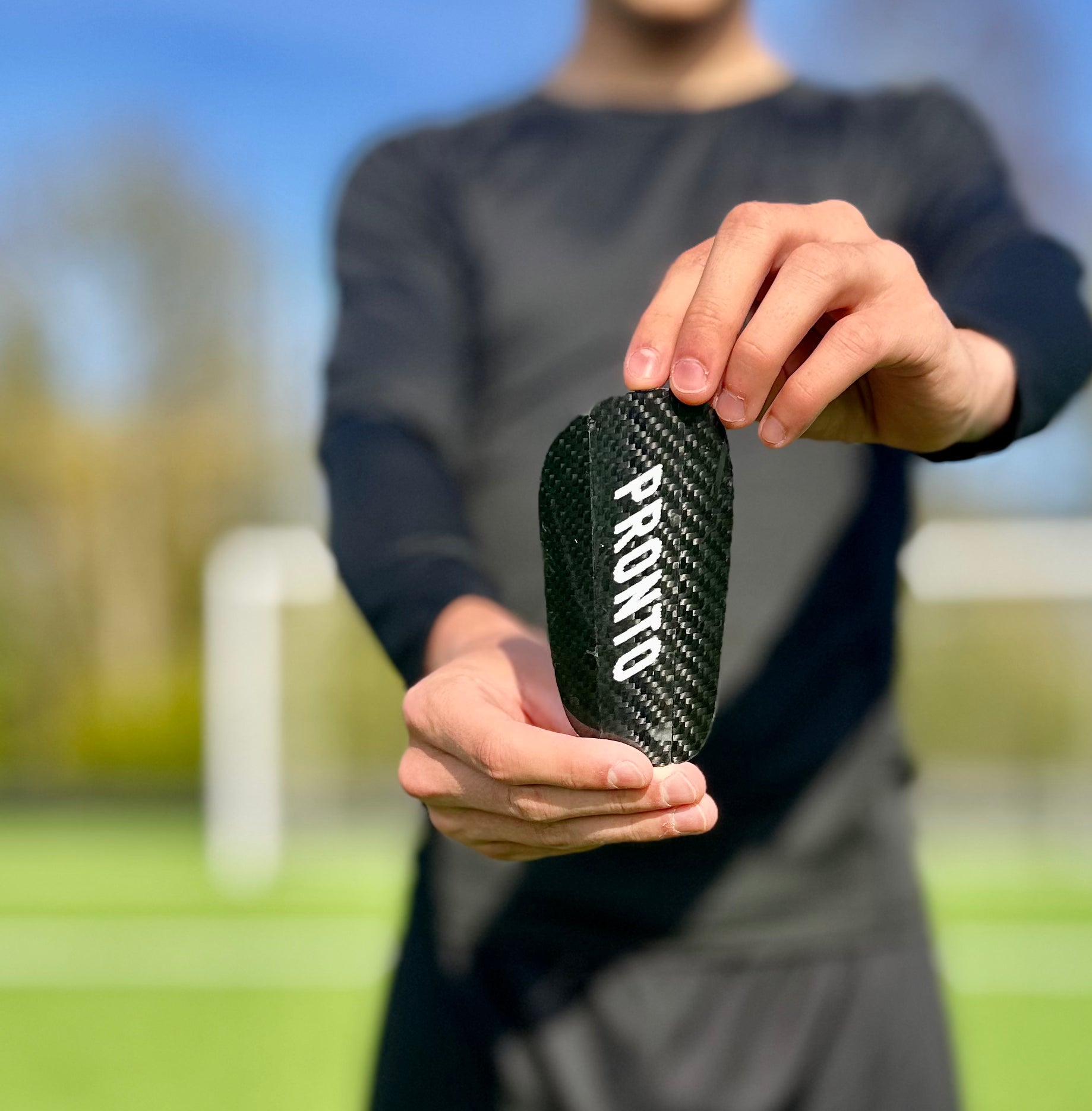 Person i sort træningstøj holder Pronto carbon benskinne foran sig på en fodboldbane